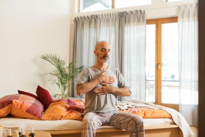 Mann praktiziert Energiearbeit auf einem Bett, f&ouml;rdert Entspannung und Achtsamkeit im sonnendurchfluteten Raum.