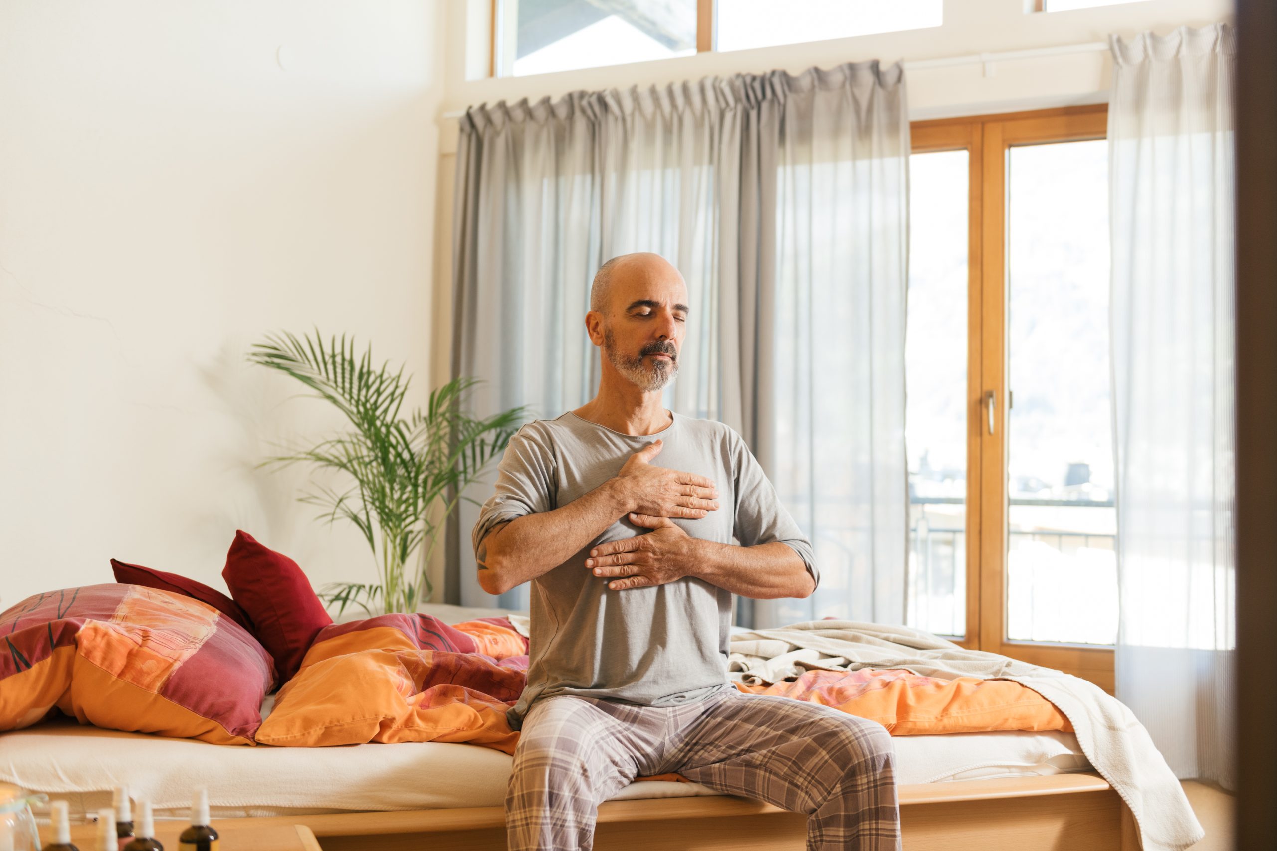 Mann praktiziert Energiearbeit auf einem Bett, fördert Entspannung und Achtsamkeit im sonnendurchfluteten Raum.