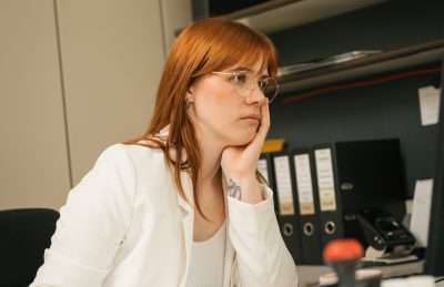 Person im B&uuml;ro gelangweilt von ihrem Job am Computer. Arbeitstische und Ordner im Hintergrund.