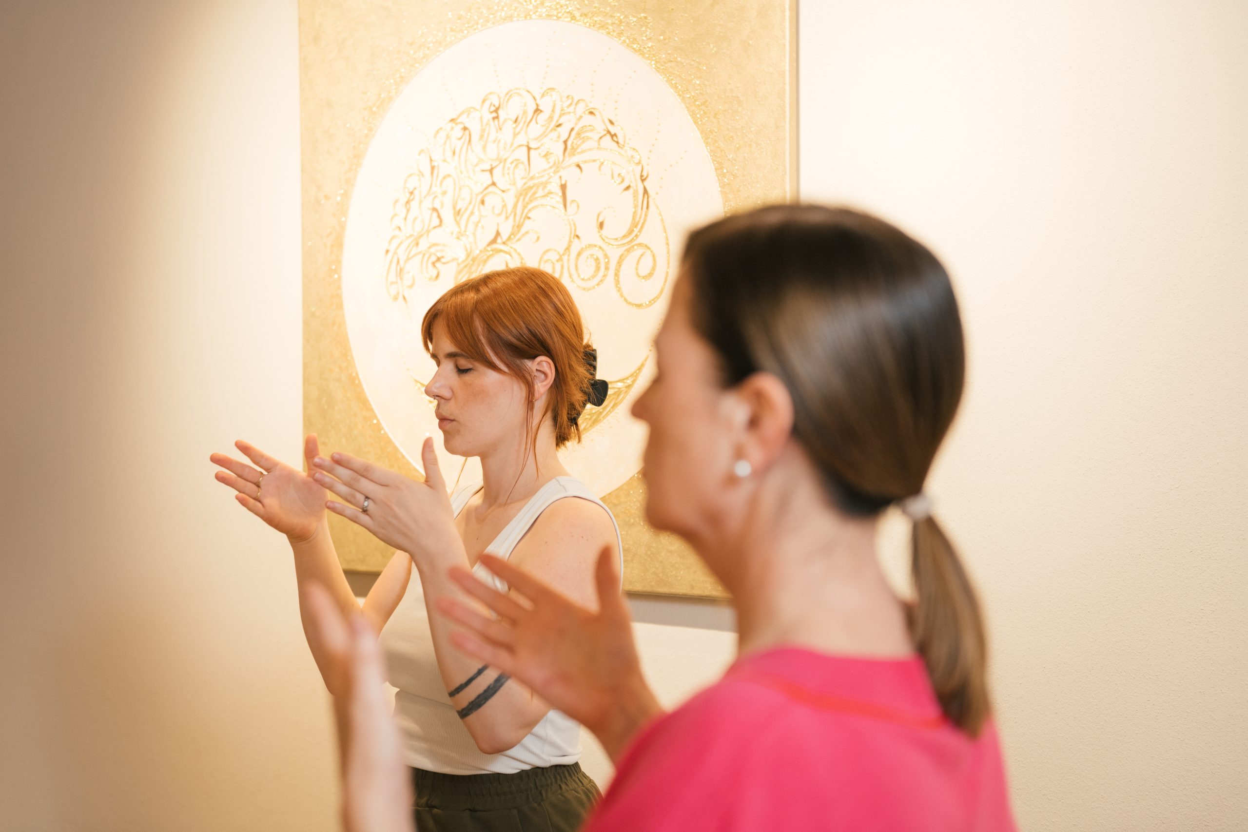 Zwei Frauen praktizieren Energiearbeit vor einem kunstvollen Wandbild, das positive Schwingungen verstärkt.