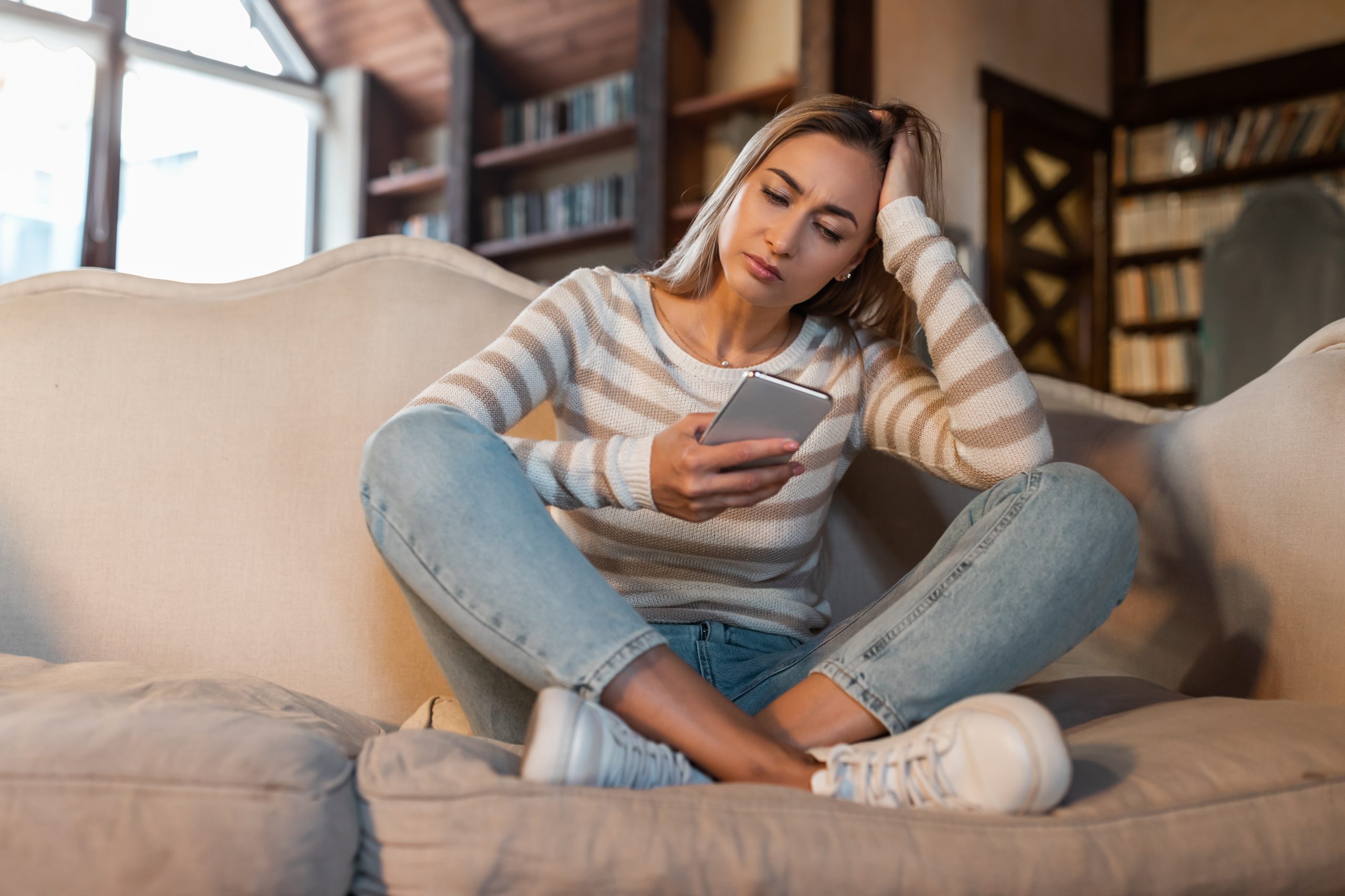 Frau auf Sofa mit Handy, nach Energiearbeit suchend, um Balance zu finden.
