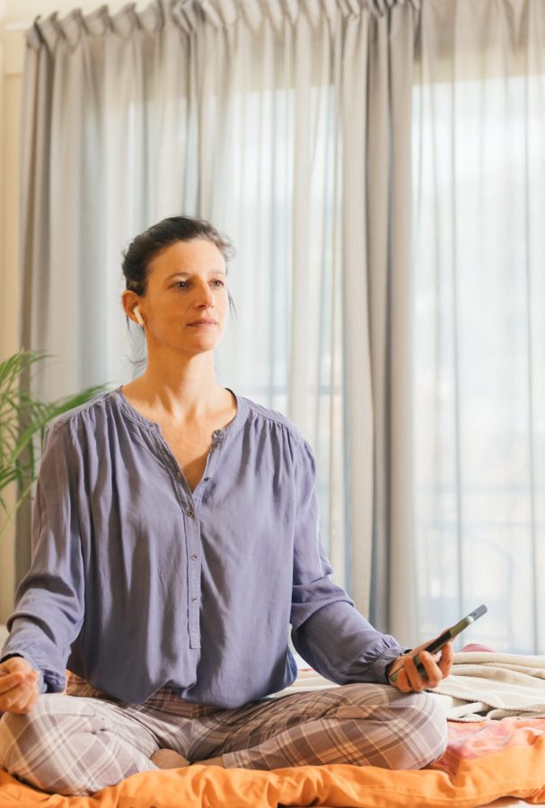 Frau praktiziert Energiearbeit durch Meditation im gem&uuml;tlichen Schlafzimmer f&uuml;r innere Ruhe und Gelassenheit.