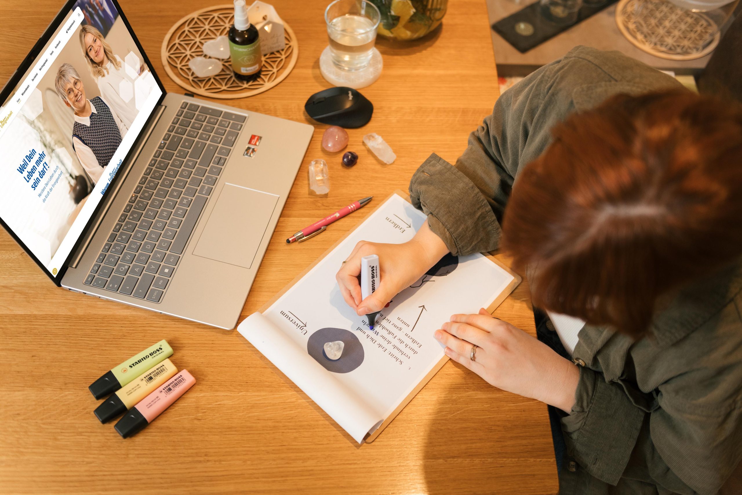 Plattform-67460 Person arbeitet an Energiearbeit, umgeben von Laptop und Kristallen auf einem Schreibtisch.