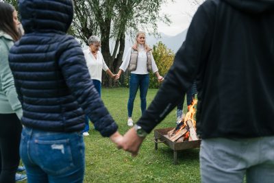 Menschen halten sich bei einem Lagerfeuer an den H&auml;nden, um Energiearbeit im Freien zu praktizieren.
