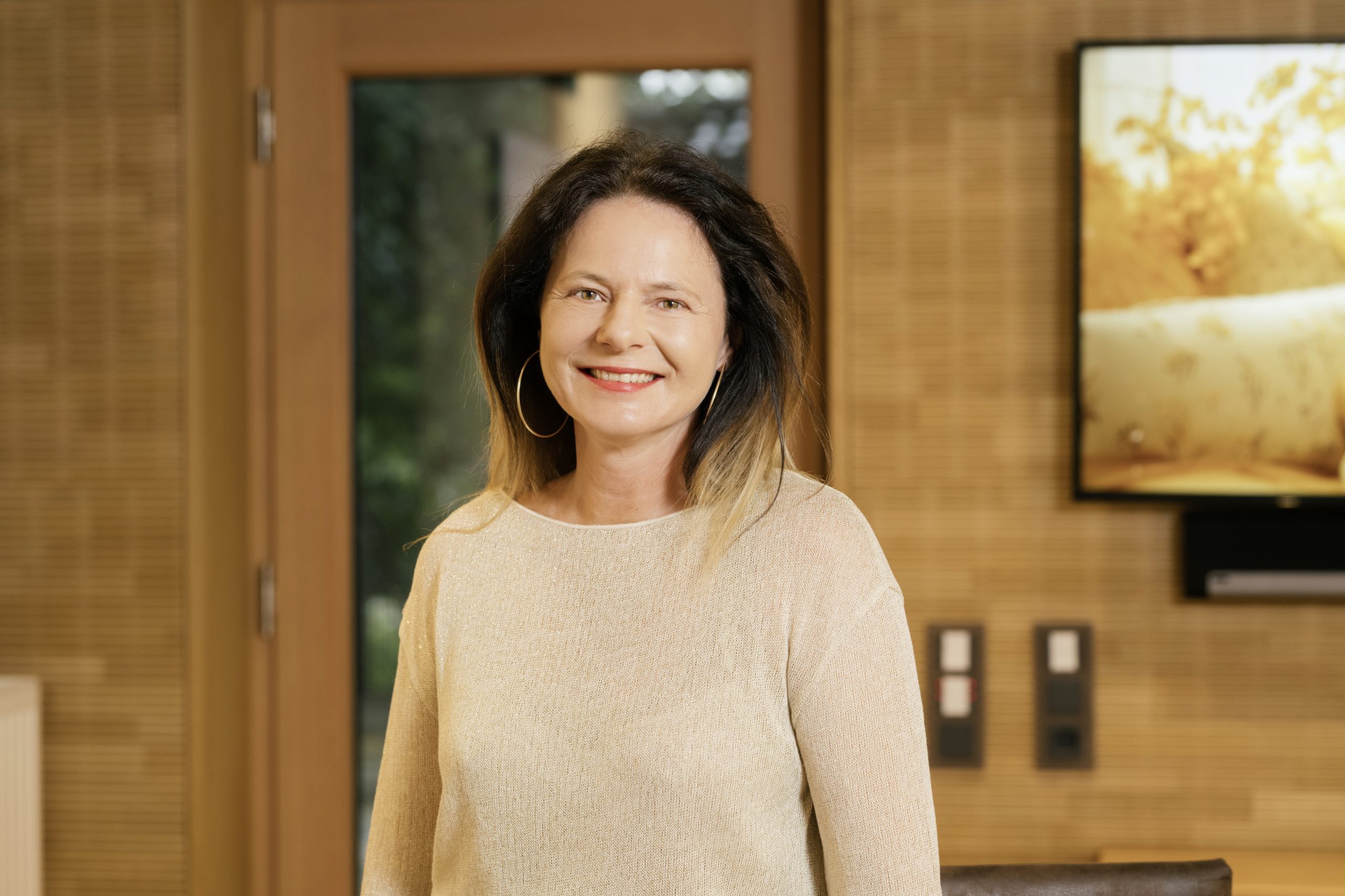 Eine Frau l&auml;chelt gelassen im Holzinterieur, Symbol f&uuml;r Energiearbeit und positive Ausstrahlung.