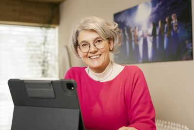 Frau in rotem Pullover lächelt vor Tablet, unterstützt von einer energetischen Gruppe als Symbol für Energiearbeit.
